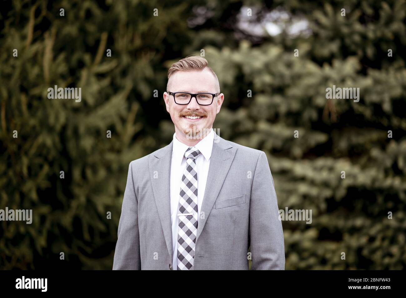 Handsome man in suit standing outdoors with blurry greenery in the background Stock Photo