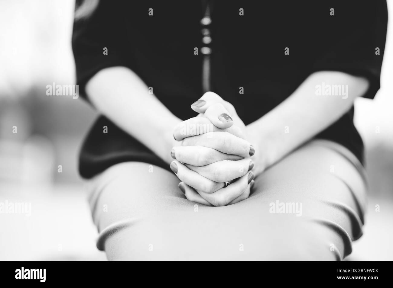 Grayscale of a woman sitting with hands together on lap while praying ...