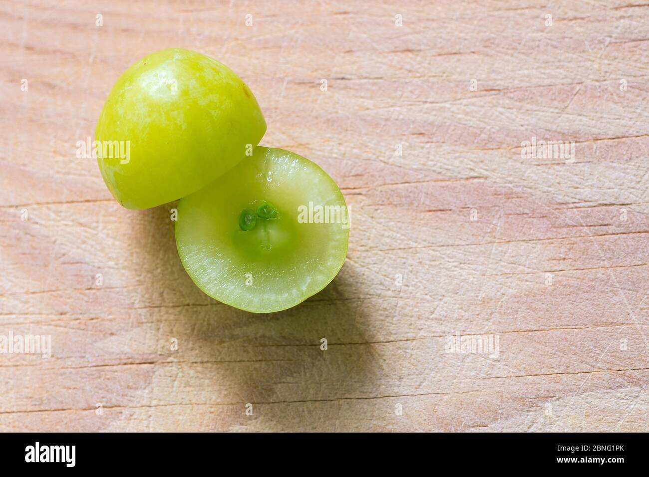 A yellow grape cut in two on a wooden board illuminated with natural light Stock Photo