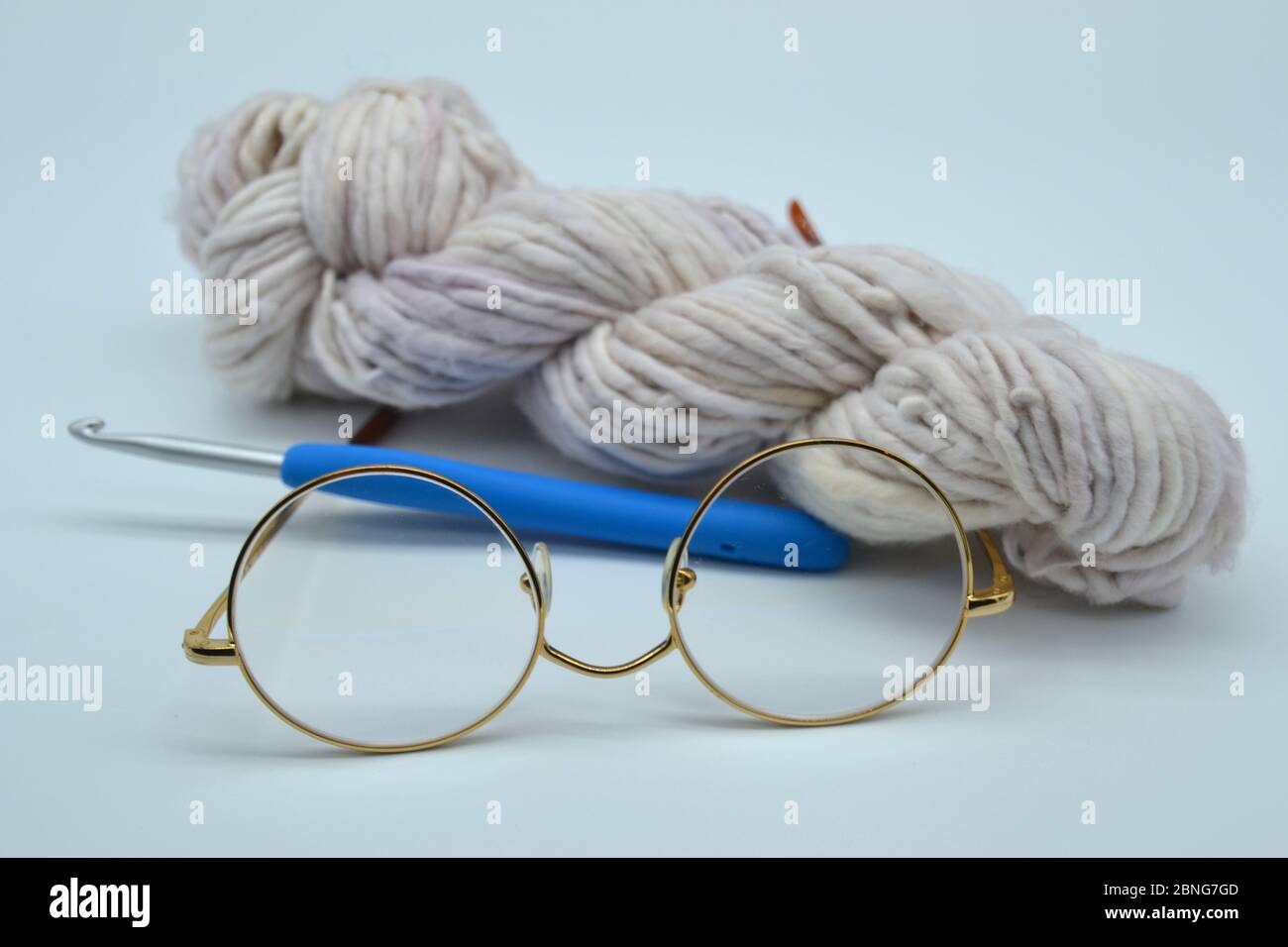 Handspun hand-dyed skein or ball of oatmeal colored yarn or wool with a crochet hook and a pair of retro gold rimmed Grandma reading glasses Stock Photo