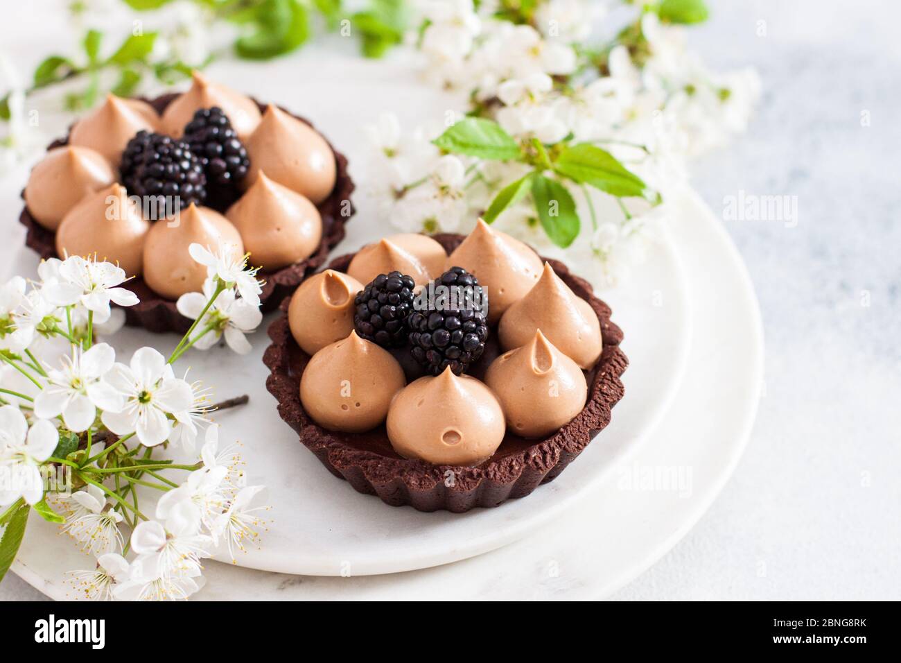 Chocolate tart with salted caramel filling and fresh blackberries. Cherry flowers on background. Copy space. Stock Photo
