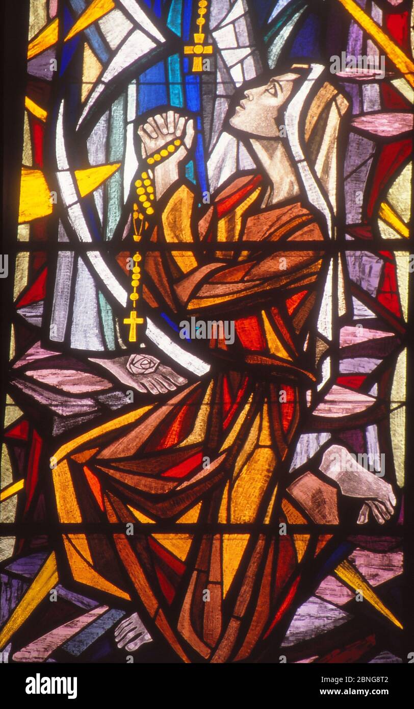 LOS ANGELES, UNITED STATES - Mar 13, 1990: Stained Glass image of St. Bernadette praying to Blessed Mother in Lourdes grotto. Stock Photo
