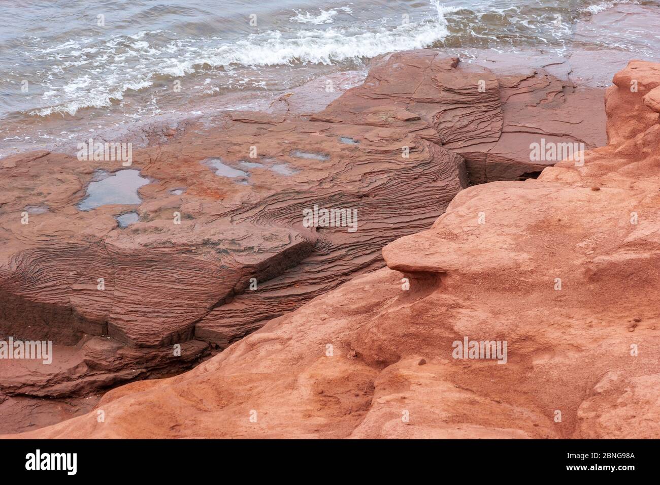 Layered red sandstone and soil under wave abrasion. Coastal erosion on