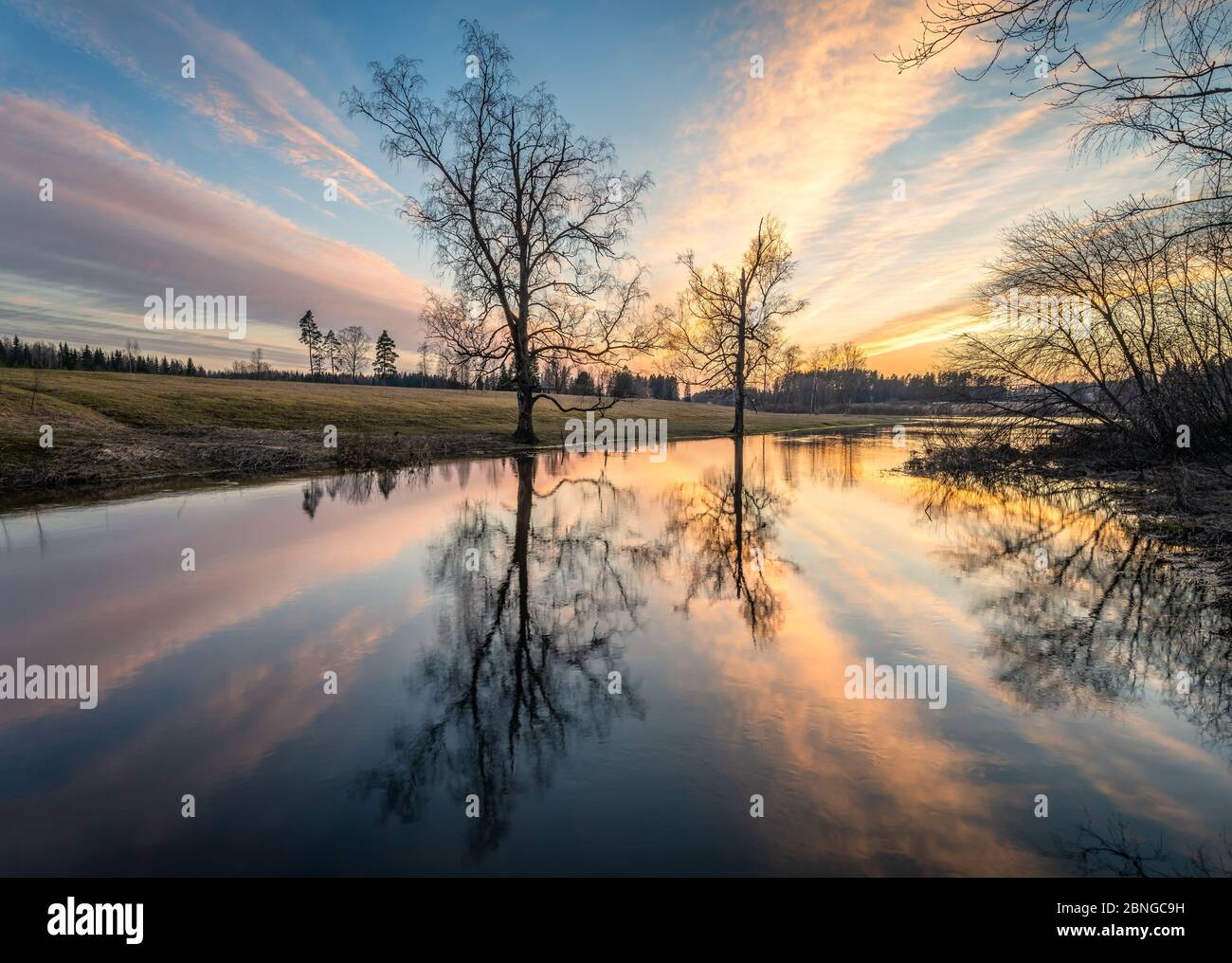 Beautiful sunset glow with calm landscape with tree reflections and sunlight at spring evening in river Finland Stock Photo