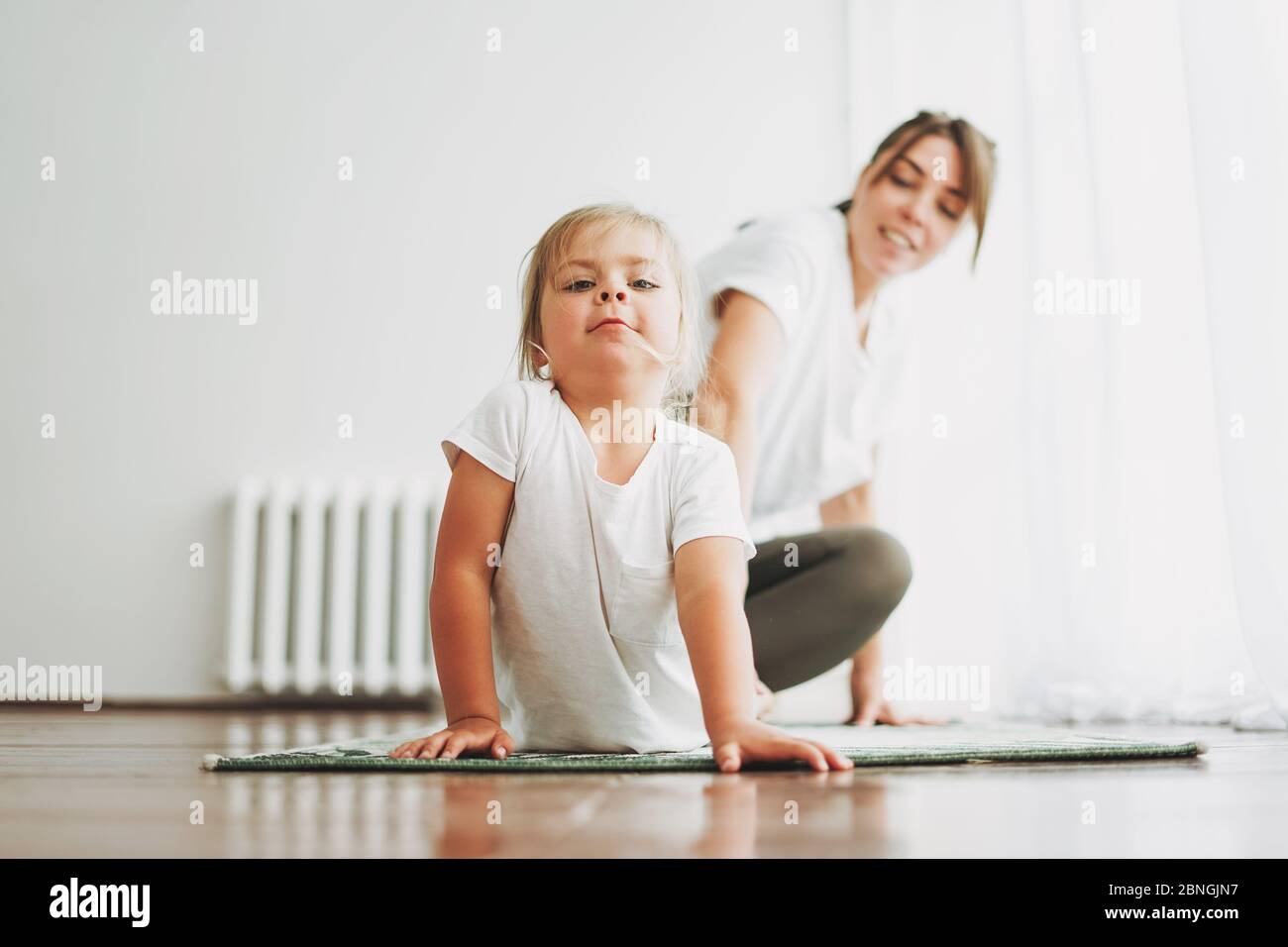 Happy mom and little daughter doing yoga morning exercise together at bright interior home Stock Photo