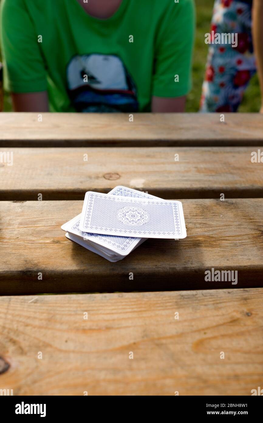 close up of a stack of playing cards on a wooden pub table with a young boy sitting in the background waiting to play Stock Photo