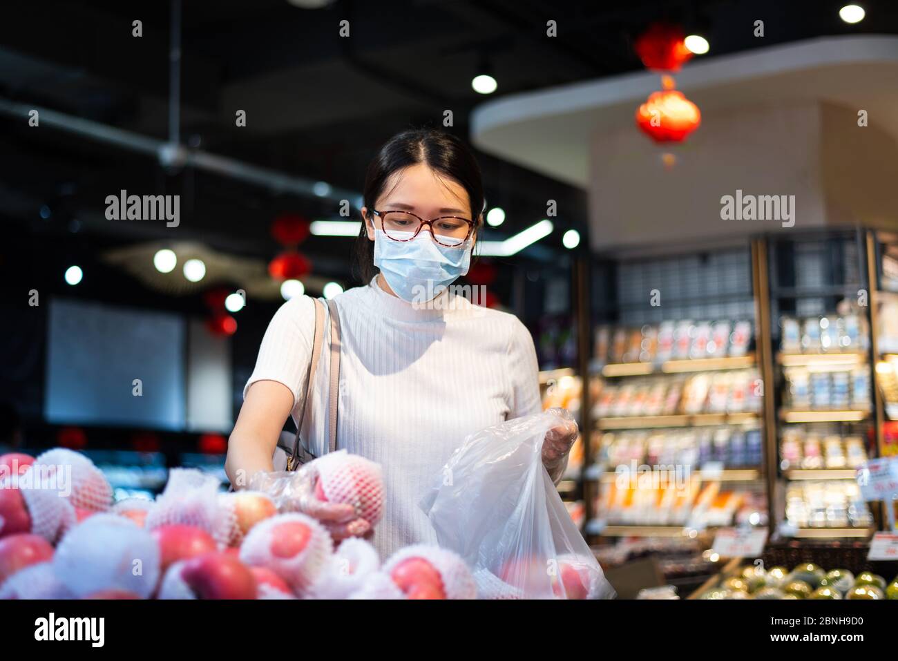 Asian woman shopping for fruit in the market wearing mask and gloves to prevent virus spread during coronavirus pandemic Stock Photo