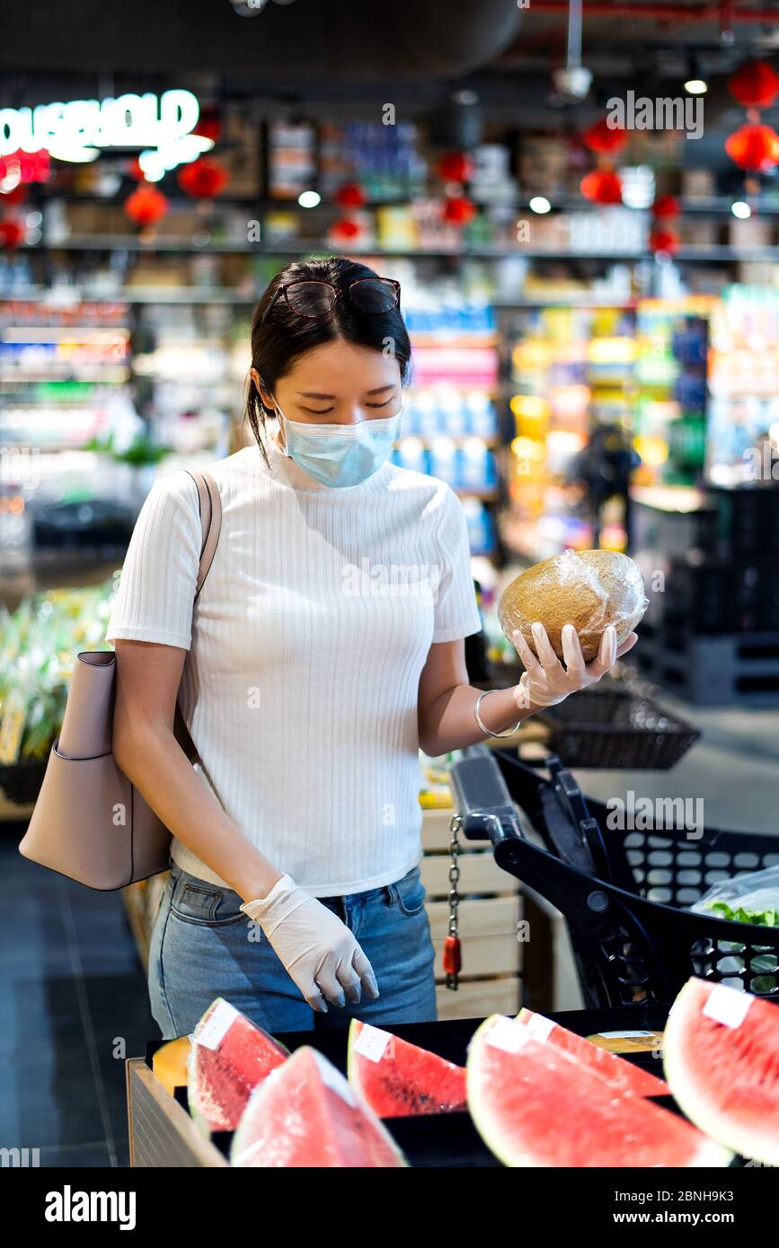 Asian woman shopping for fruits in the market wearing mask and gloves to prevent virus spread during coronavirus pandemic Stock Photo