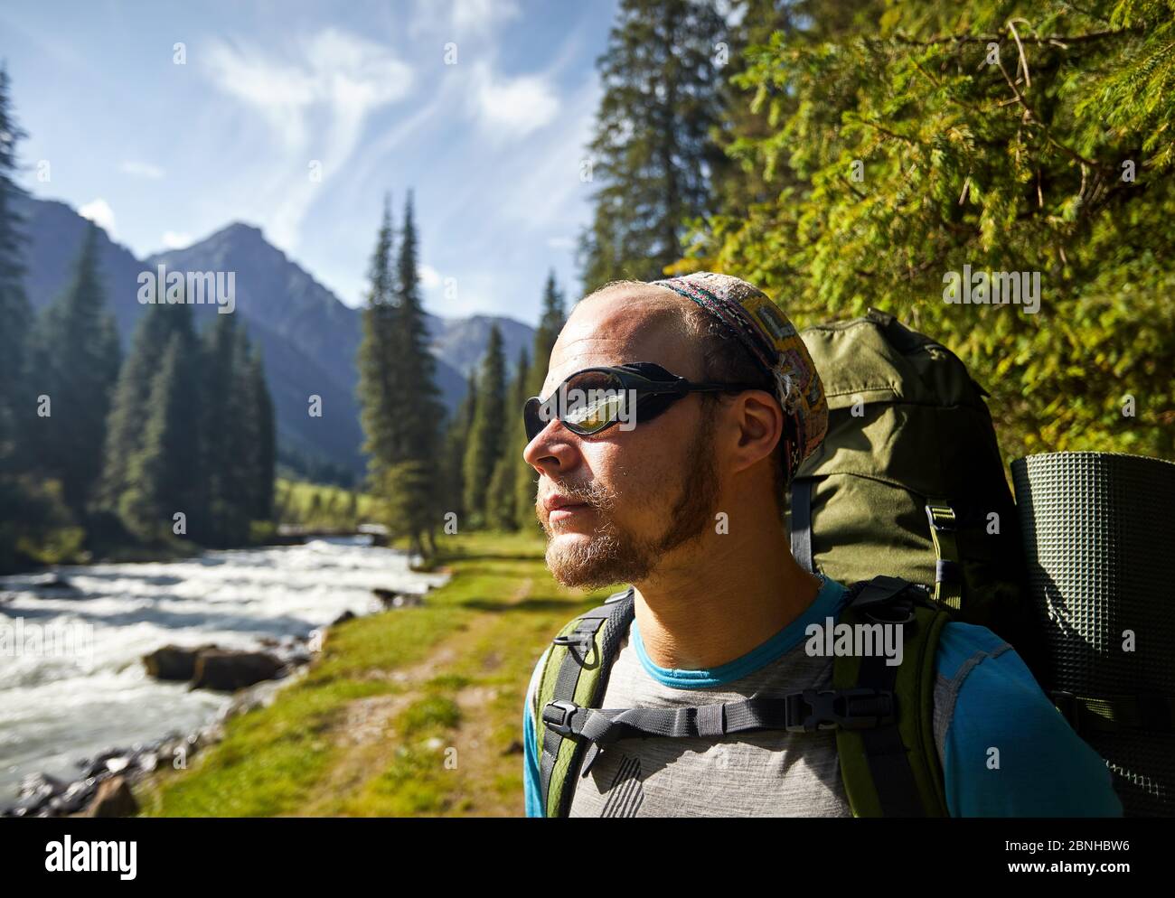 Portrait of hiker with big backpack and sunglasses near the river mountain valley in Karakol national park, Kyrgyzstan Stock Photo
