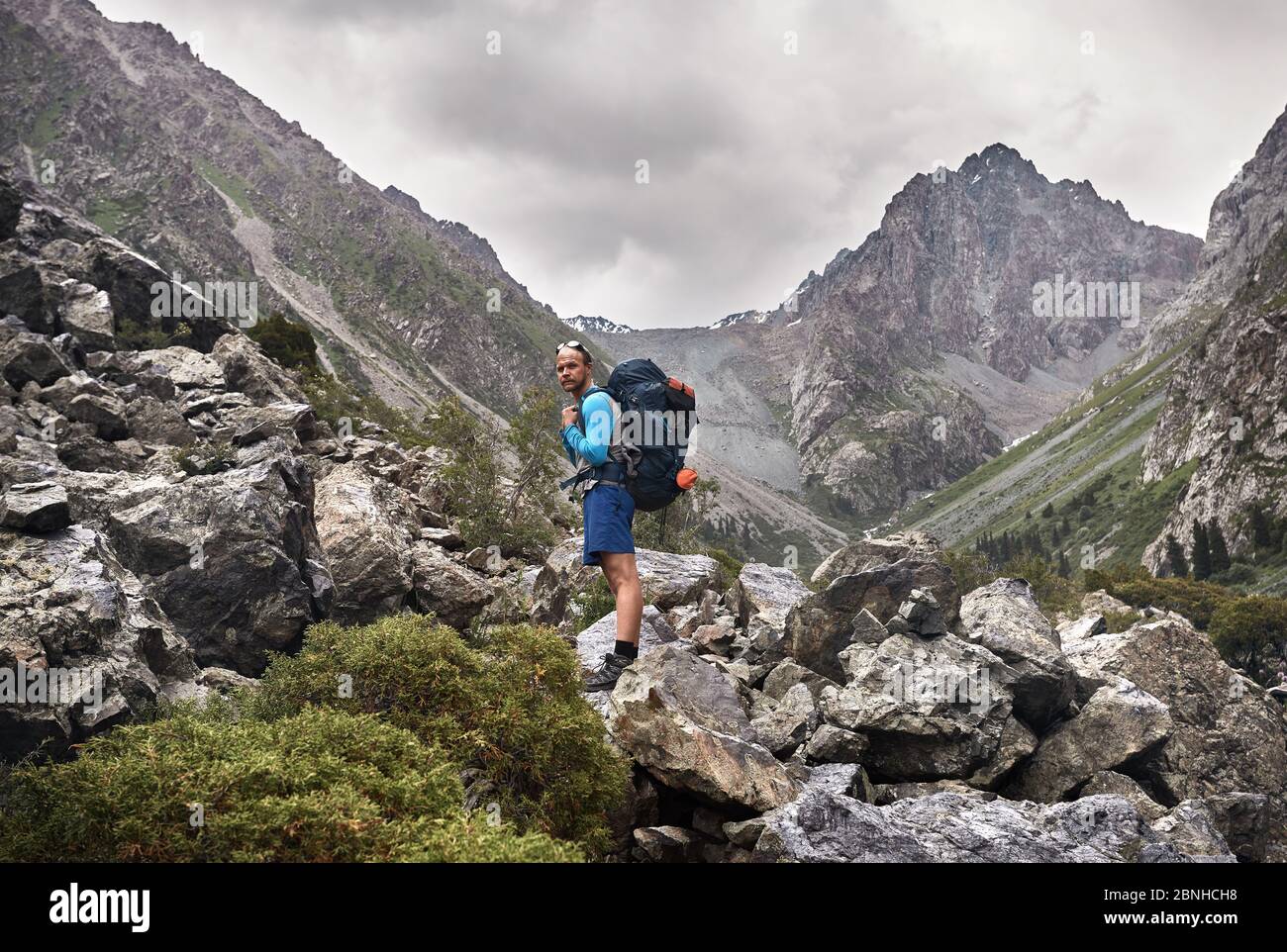 Portrait of tourist with big backpack is on the rocky trail in the mountain valley of Karakol national park, Kyrgyzstan Stock Photo
