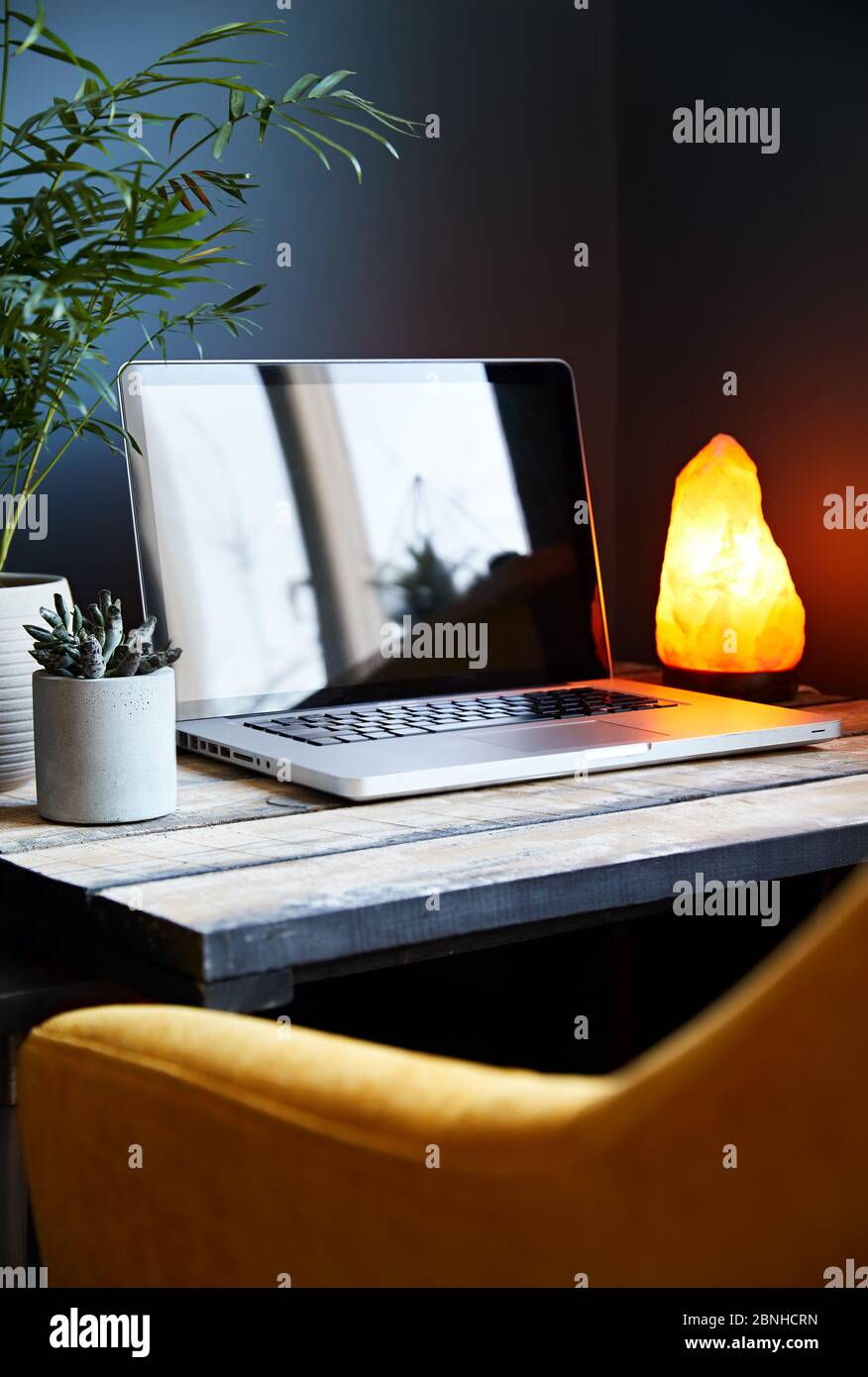 Cozy workspace with laptop yellow glowing lamp and chair at stone grey wall background. Working from home concept. Stock Photo