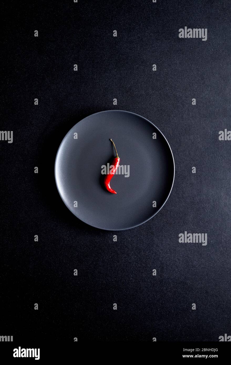 Minimalist composition of red chili pepper in black ceramic plate at black table Stock Photo