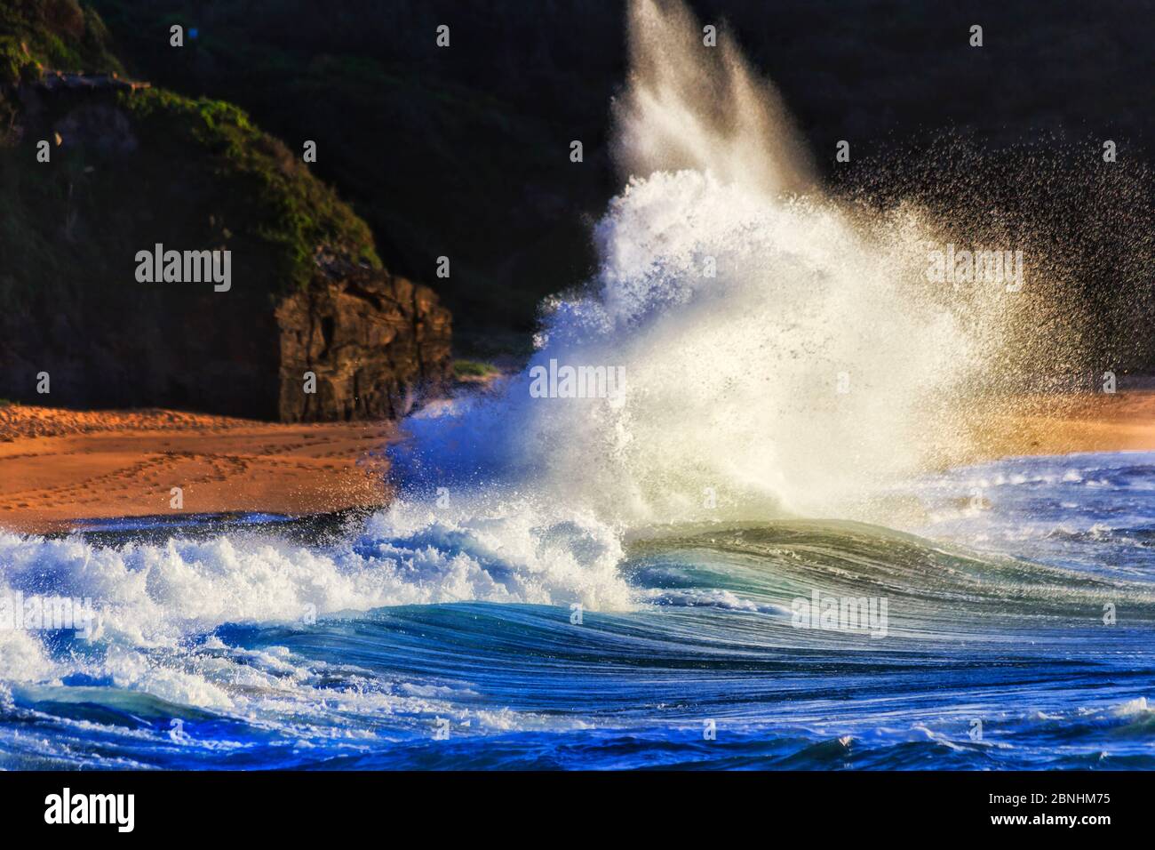 Strong powerful wave rolling on shore of Sydney Northern beaches at sunrise against dark headland. Stock Photo