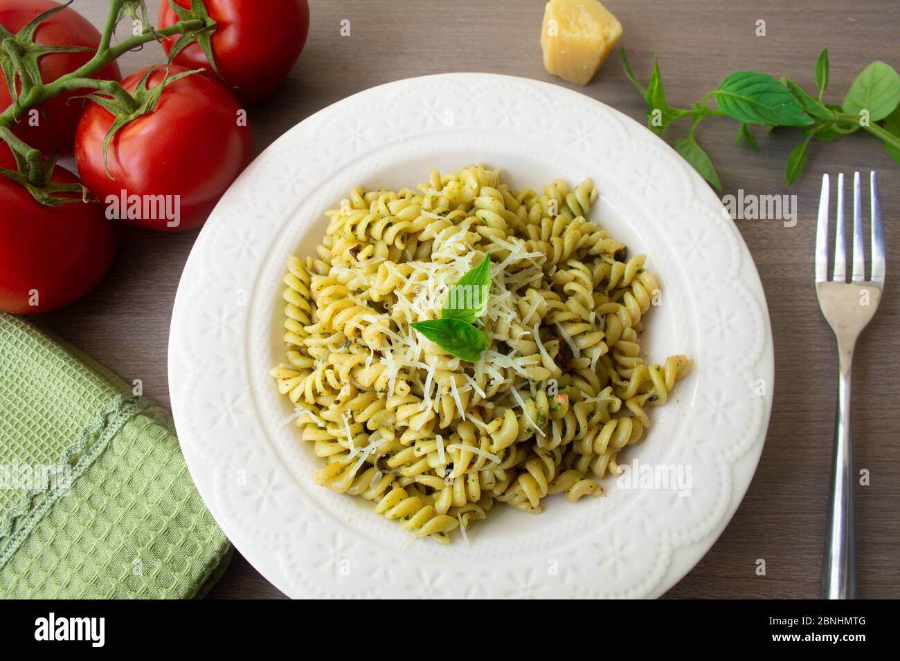 Traditional Italian vegetarian pasta fusilli with fresh homemade basil and pine nut pesto sauce and topped with grated Parmesan cheese. Tomato, basil, Stock Photo