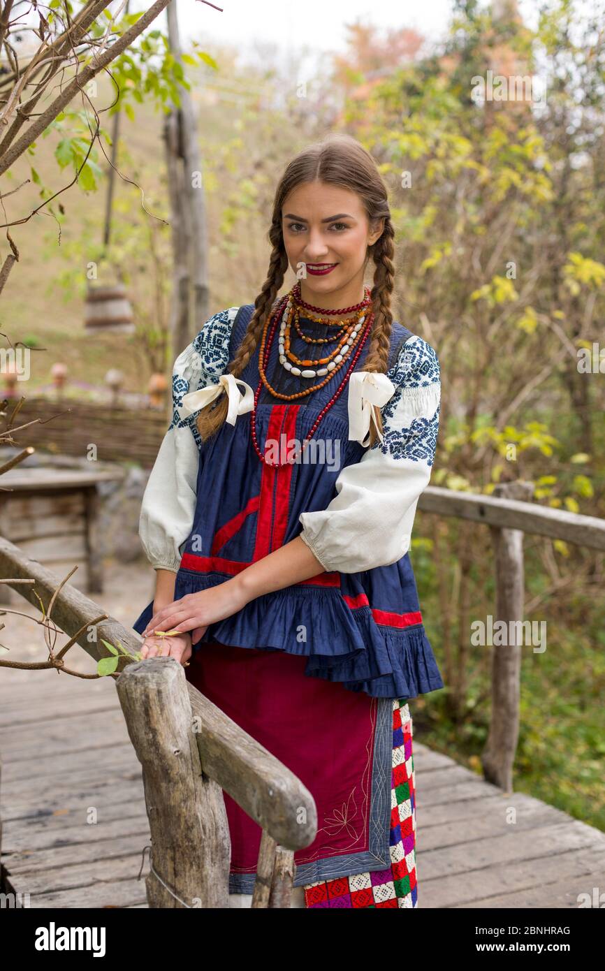 A girl in national dress is walking through an old bridge. Old clothes. Retro staging of an ancient rite. Beautiful dress and skirt on a woman. Beads Stock Photo