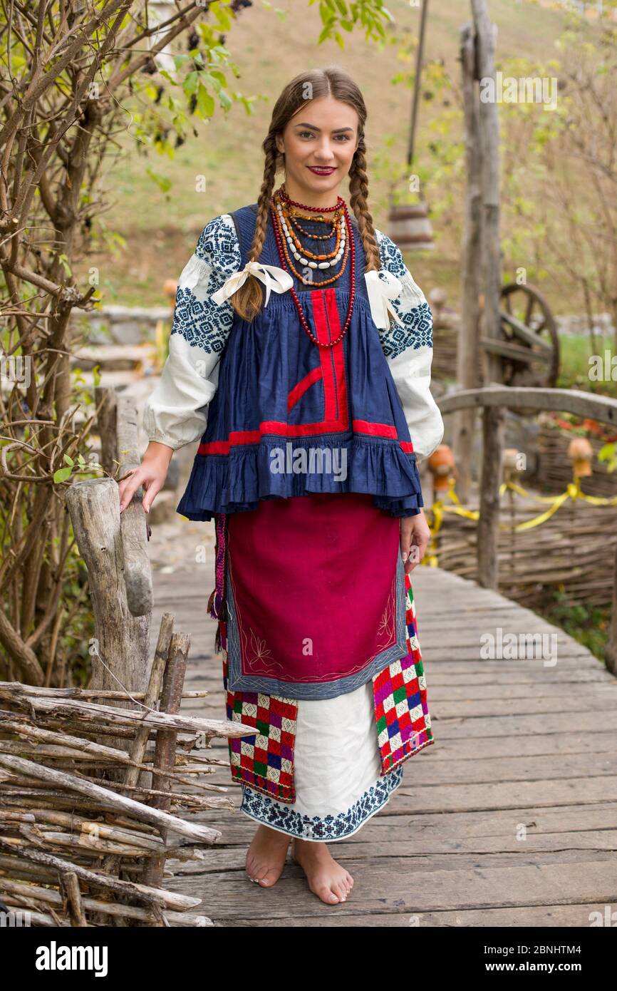 A girl in national dress is walking through an old bridge. Old clothes. Retro staging of an ancient rite. Beautiful dress and skirt on a woman. Beads Stock Photo