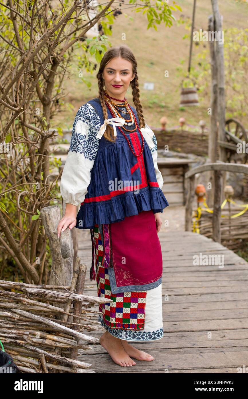 A girl in national dress is walking through an old bridge. Old clothes. Retro staging of an ancient rite. Beautiful dress and skirt on a woman. Beads Stock Photo