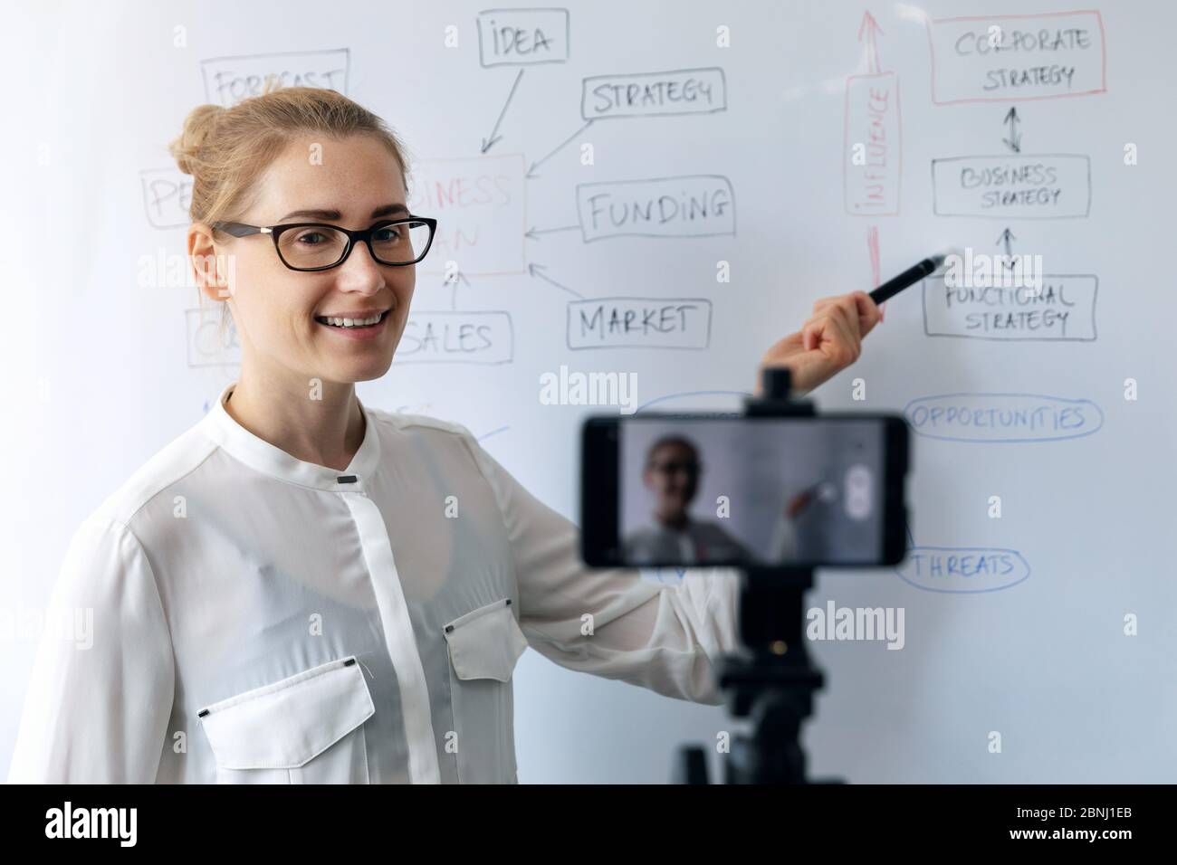 online education, webinar and business vlog concept - woman teaching and recording video with phone in front of whiteboard Stock Photo