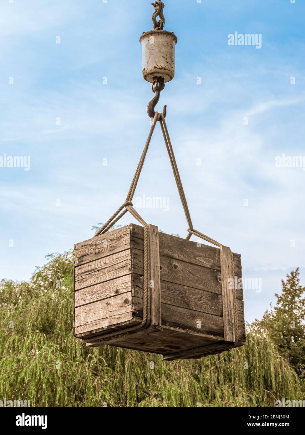 Wooden box hanging on the hook of a crane. Stock Photo
