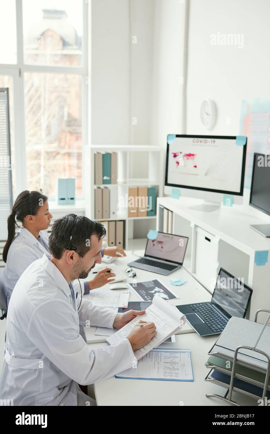 Two doctors sitting at the table and making notes in documents together during their work at office Stock Photo
