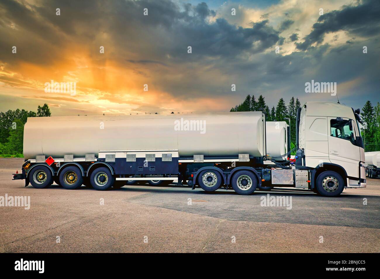 White semi tanker truck parked on asphalt yard, side view, with beautiful sunset sky on the background. Recognisable elements removed. Stock Photo