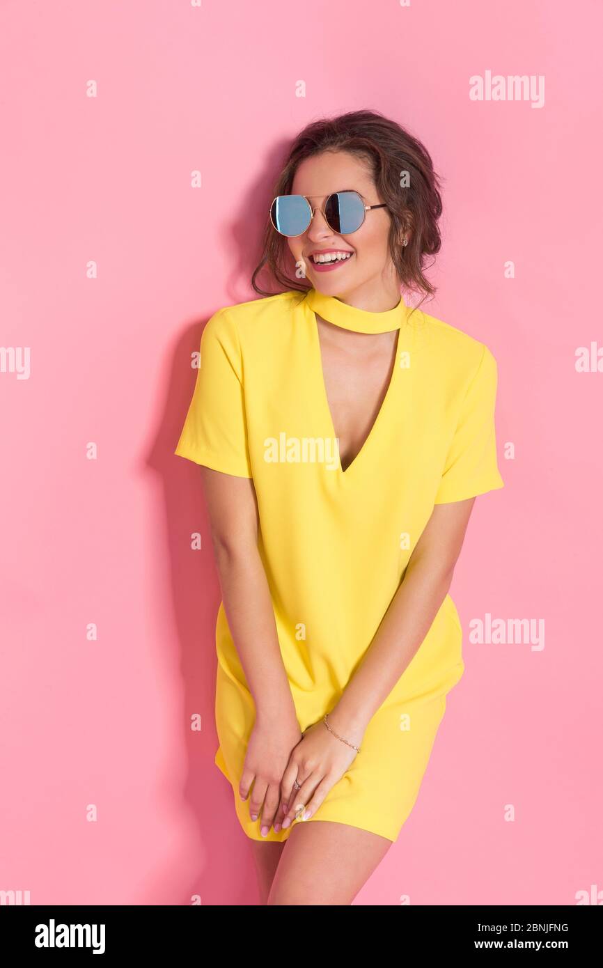 Beautiful girl wearing yellow dress and sunglasses posing on pink
