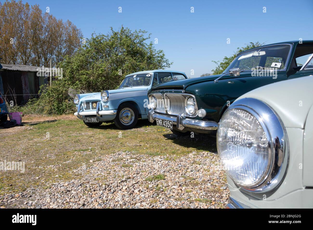A row of beautiful classic cars, looking at the front from the side. Glistening in the sun on a bright, sunny day Stock Photo
