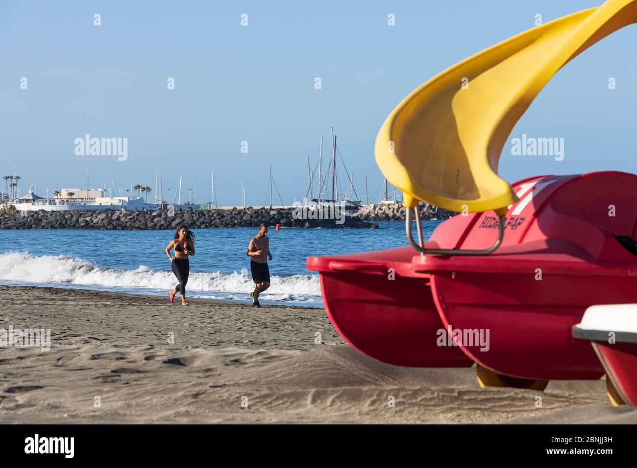 Costa Adeje, Tenerife, Canary Islands, Spain. 15 May 2020. Playa Fañabe beach opens for limited exercise and sports activities. Walking, running are allowed but no sunbathing, water sports or swimming under the de-escalation of the Covid 19, Coronavirus lockdown. Runners on the shore. Stock Photo