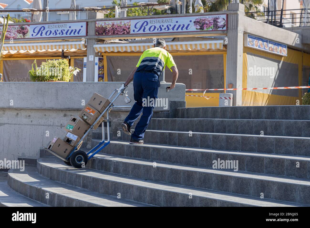 Costa Adeje, Tenerife, Canary Islands, Spain. 15 May 2020. Playa Fañabe beach opens for limited exercise and sports activities. Walking, running are allowed but no sunbathing, water sports or swimming under the de-escalation of the Covid 19, Coronavirus lockdown. Delivery man bringing merchandise to a beach bar which is open. Stock Photo