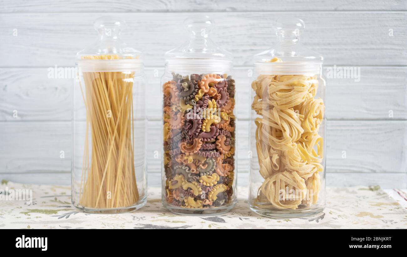 Three glass bottles with different pasta types. Pasta at home on white