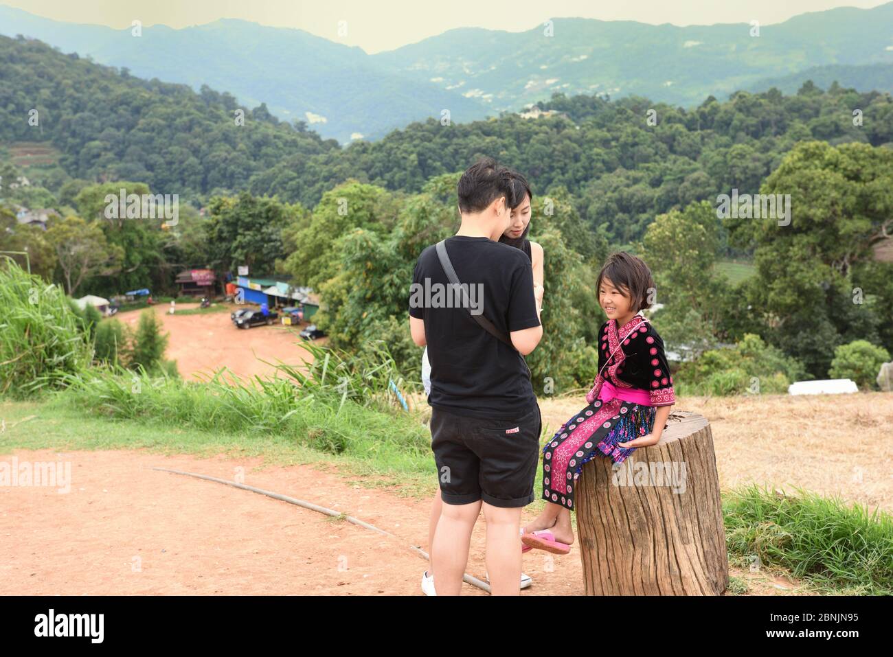 Tourists talking to a young Hmong girl wearing traditional dress at the mountain viewpoint of Mon Cham,Chiang Mai Province, Thailand Stock Photo