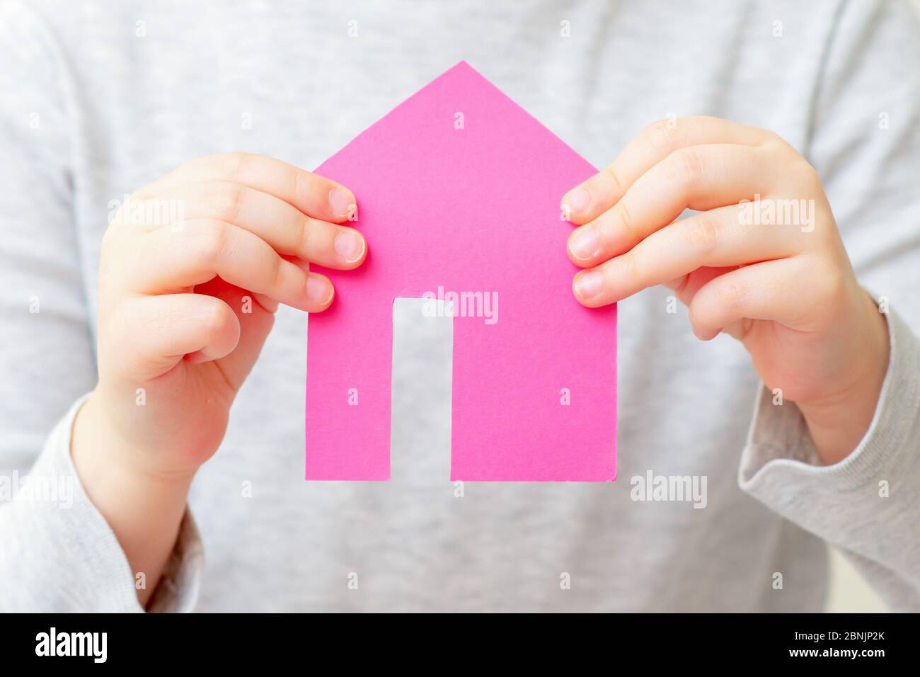 Closeup of hands of child holding paper pink house on white bachground. Housing and family concept. Stock Photo