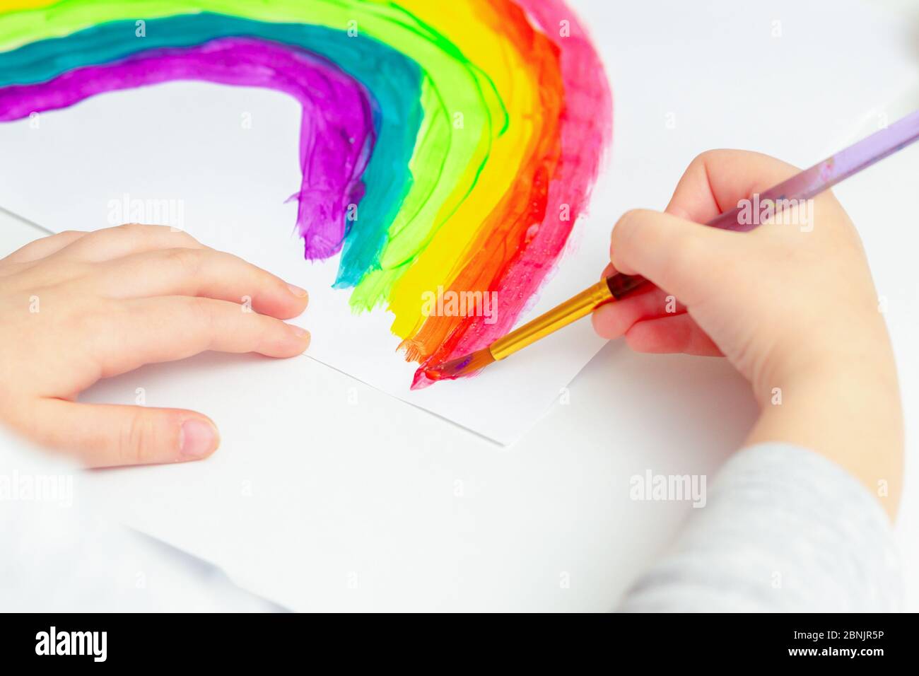 Close up of hands of a child drawing a rainbow on white paper in 