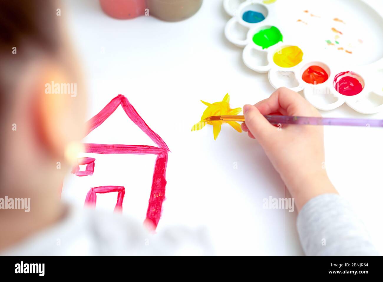 Top view of little hand of child drawing house and sun by watercolors. Education and school concept. Stock Photo