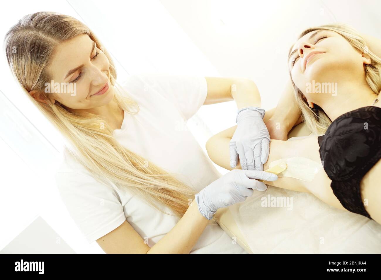 Waxing woman armpit with spatula. Salon wax beautician epilation