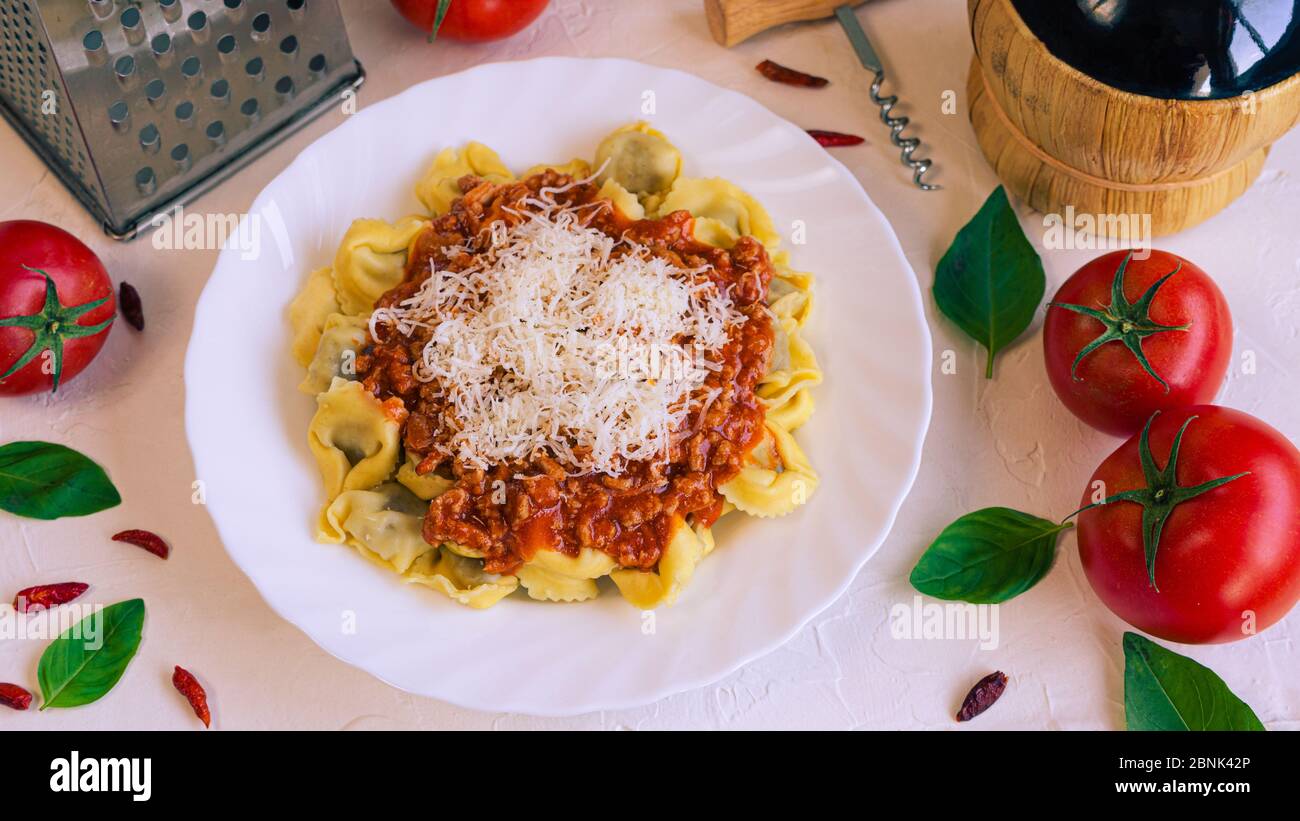 a plate full of Italian pasta accompanied by tomatoes, basil and a bottle of muscat wine Stock Photo