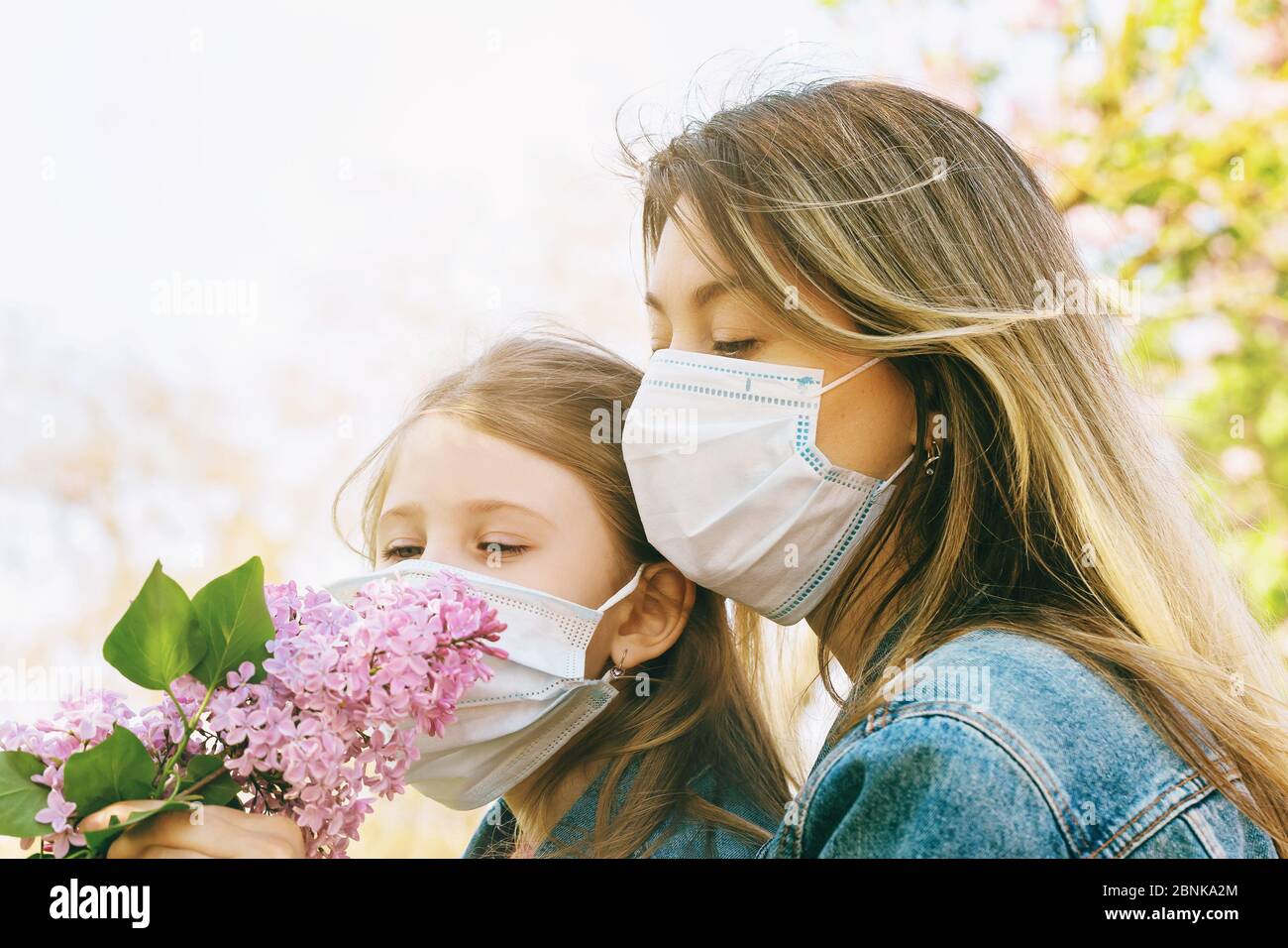Mom and daughter in medical masks sniff a lilac on the street. Quarantine exit concept Stock Photo