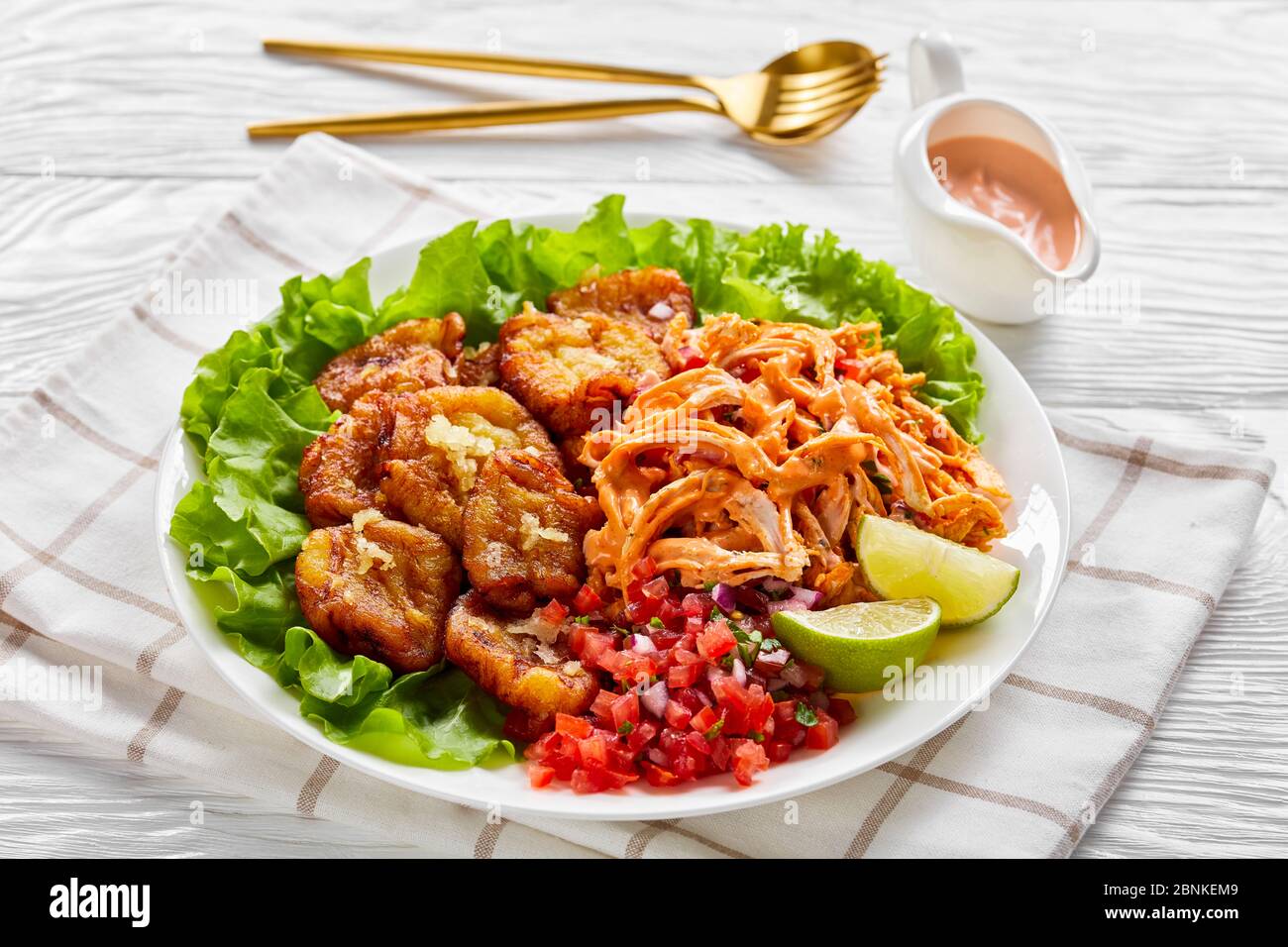 Spicy fried plantains with shredded chicken mixed with buffalo sauce, pico de gallo salsa, lime wedges on fresh lettuce leaves, on a white plate on a Stock Photo