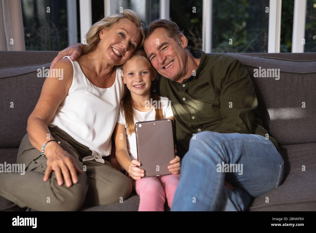 Portrait of a Caucasian girl and her grandparent using a digital tablet on a couch Stock Photo