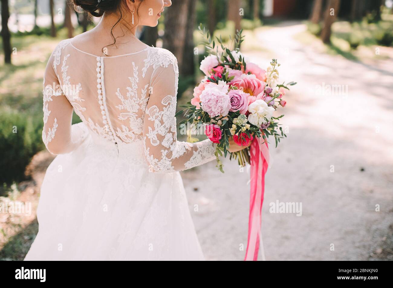 Close-up of a bride's bouquet of peonies, roses, eucalyptus in white-pink shades tied with pink ribbons. The bride holds a bouquet in her hand in a wh Stock Photo