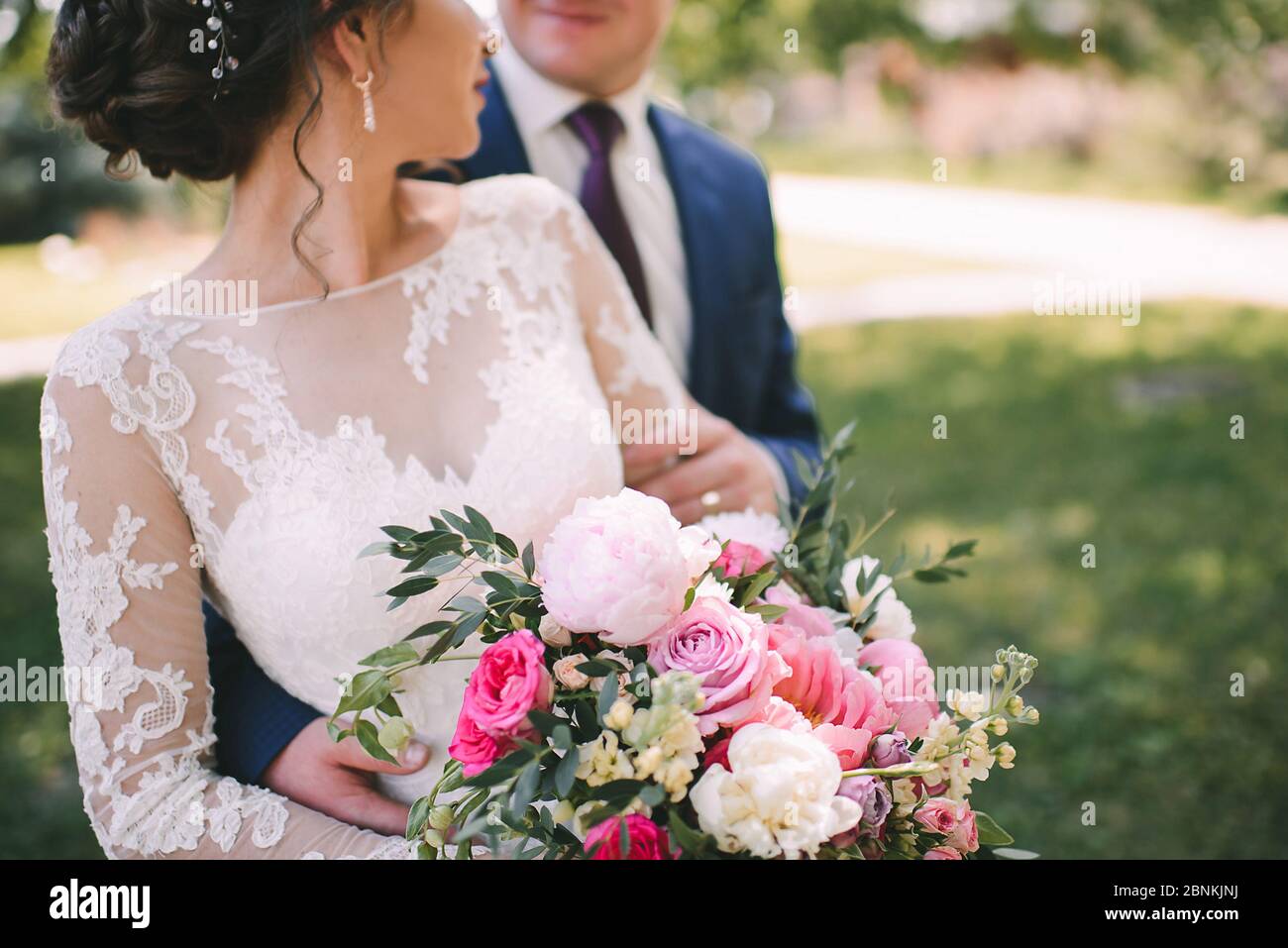 Close-up of a bride's bouquet of peonies, roses, eucalyptus in white-pink shades tied with pink ribbons. The bride holds a bouquet in her hand in a wh Stock Photo