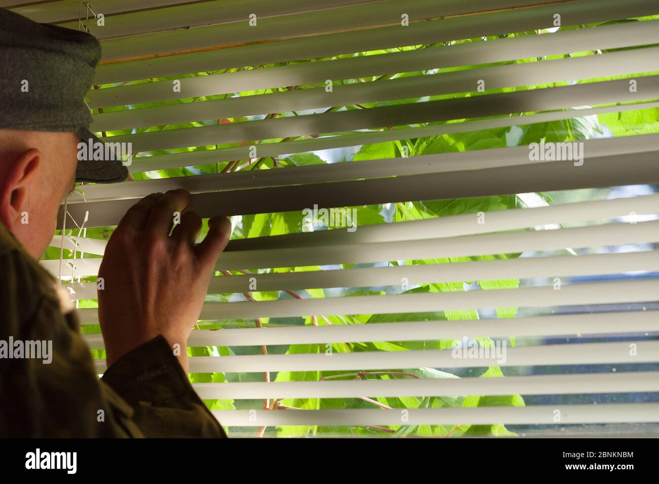 Man in uniform peeking throngh the window blinds, indoor closeup Stock Photo