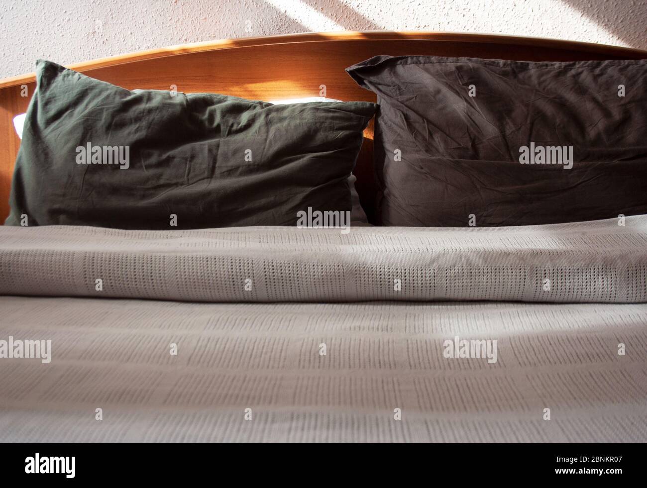 Bed linen detail with sunlight and shadows on white cotton blanket and dark grey pillows Stock Photo