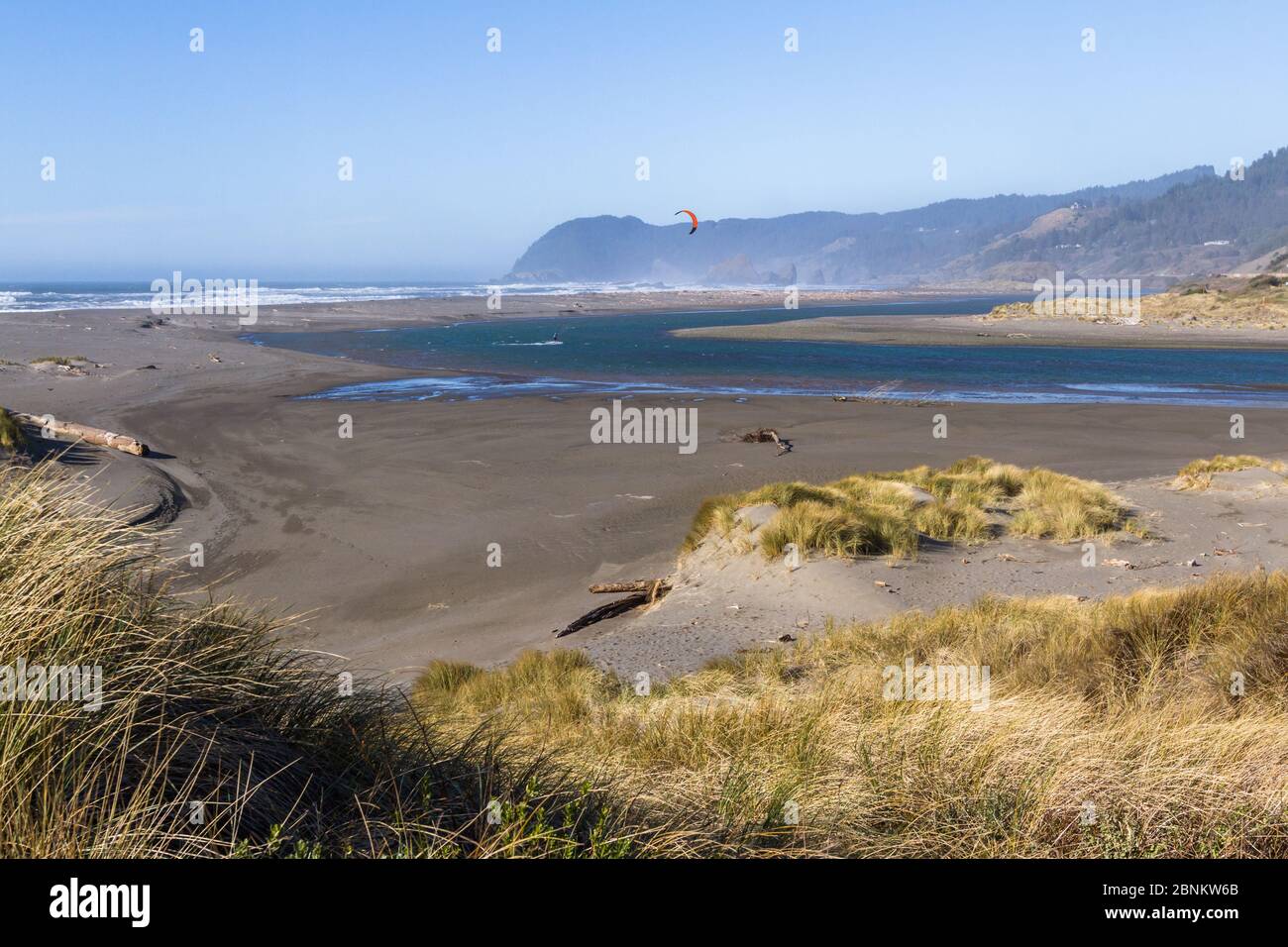 Man kite surfing in the mouth of the Pistol River with a rugged coast