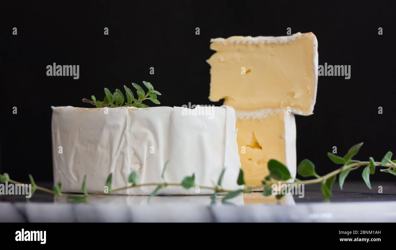 Round Brie cheese with a section cut out on a marble tray. Fresh