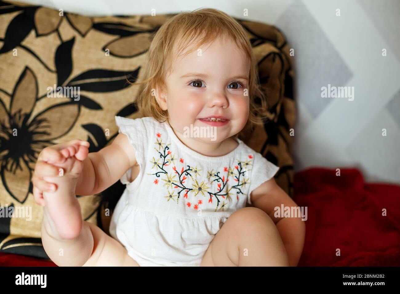 A 2 years old girl is sitting on the bed and smiling. The child rejoices and turns over. Happy