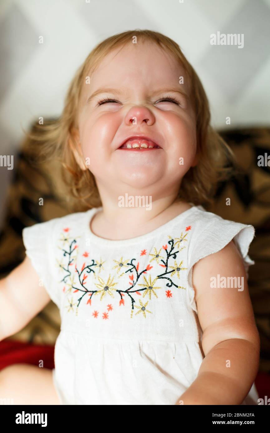 A 2 years old girl is sitting on the bed and smiling. The child rejoices and turns over. Happy