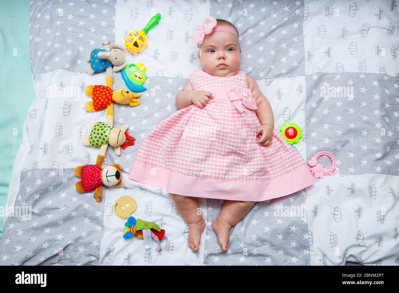 Baby girl 3 months old is lying on the bed. Baby in a pink dress