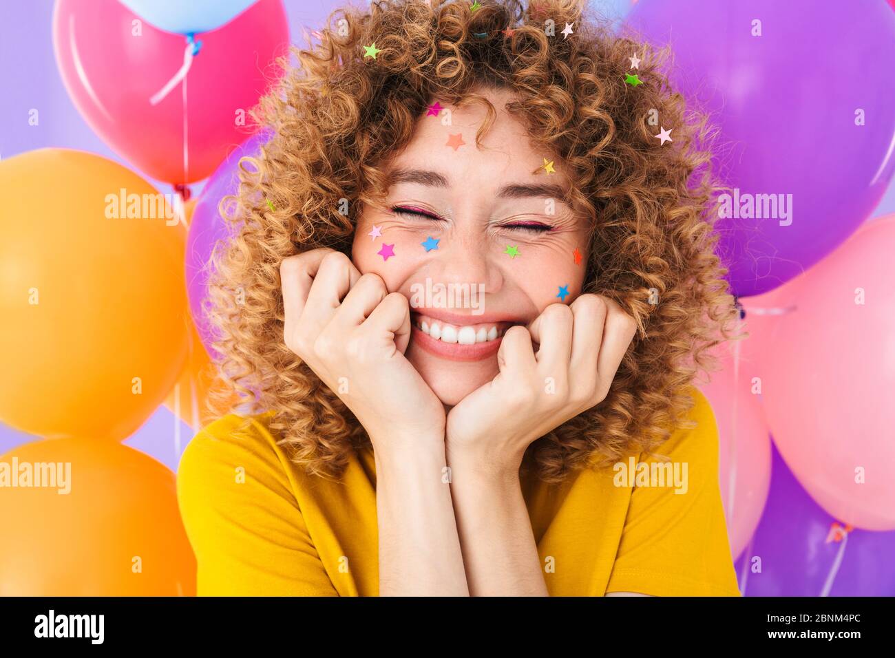 Image closeup of happy curly girl rejoicing with glitter stars on her face and multicolored air