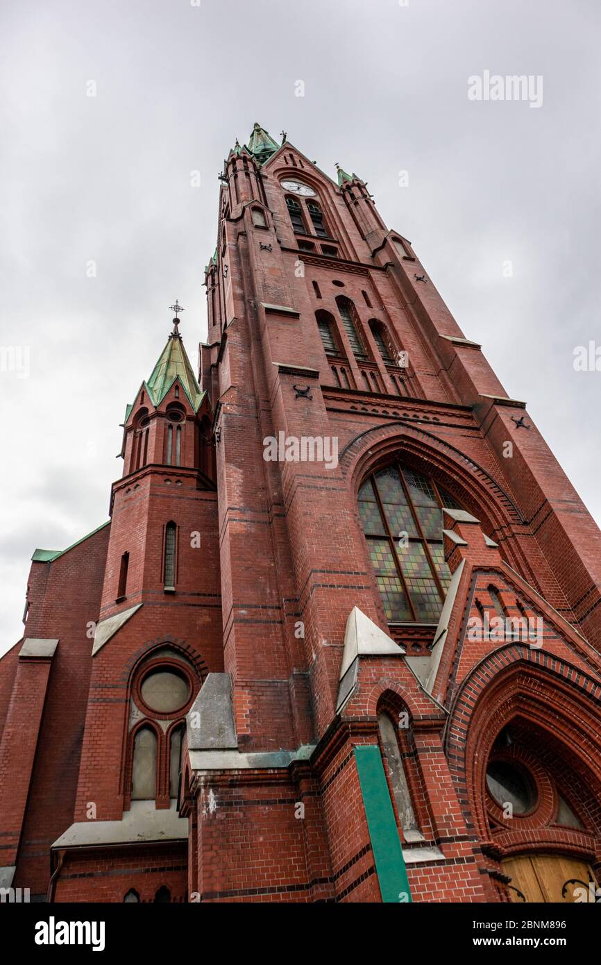 Vertical photo of high St. John's Church (Johanneskirken) in Bergen, Norway. Gothic-revival church with red brick & copper details. Cloudy day city to Stock Photo